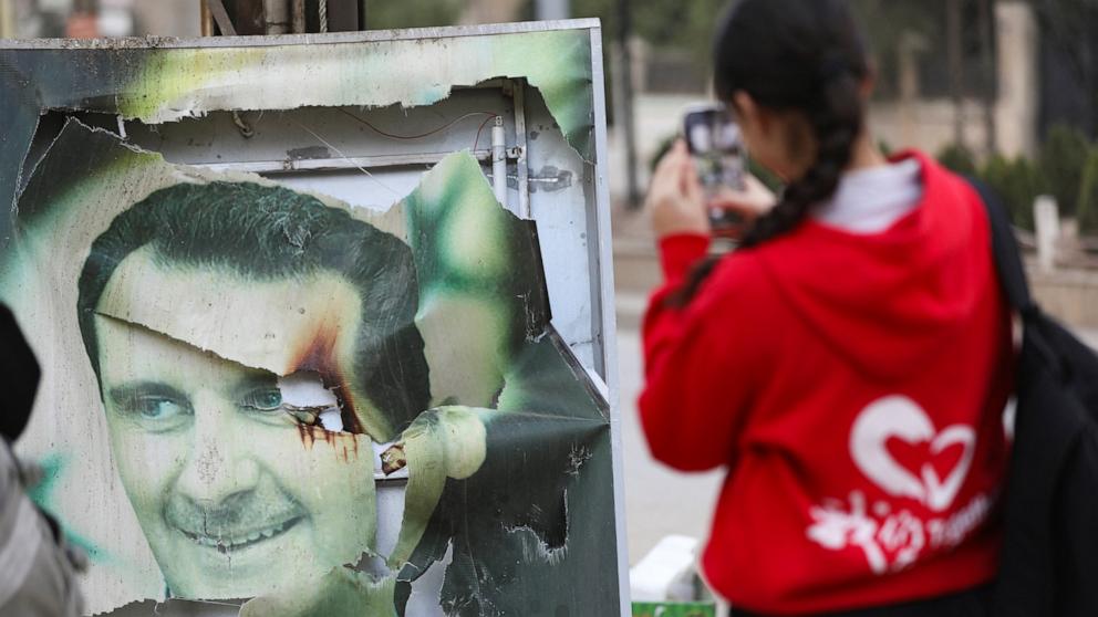 PHOTO: A woman photographs a damaged picture of Syrian President Bashar al-Assad as people celebrate his ousting by rebel forces in Qamishli, Syria, on Dec. 8, 2024.