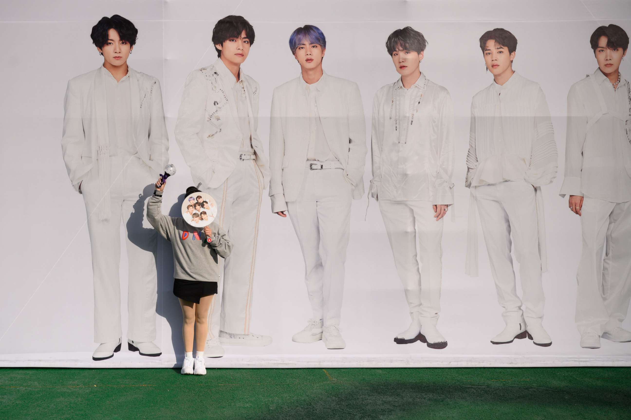 PHOTO: In a photo taken on October 29, 2019, a fan of BTS poses against a backdrop featuring an image of the band members, as they arrive for the final concert of their world tour at the Olympic stadium in Seoul. (Photo by ED JONES/AFP via Getty Images)