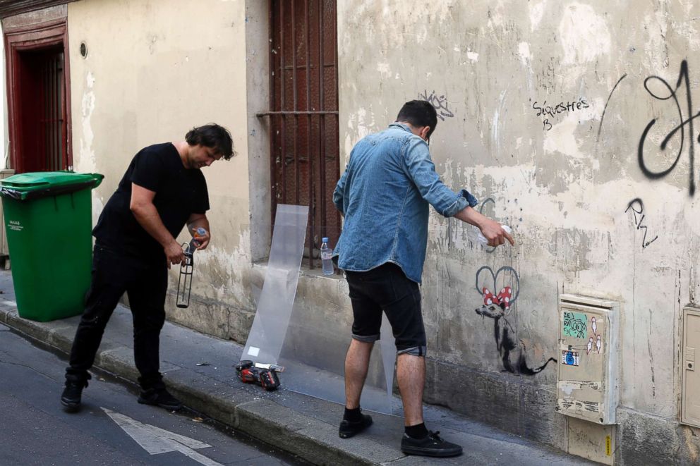 PHOTO: Two men place a protective board over a graffiti believed to be attributed to street artist Banksy, in Paris, on June 25, 2018. 