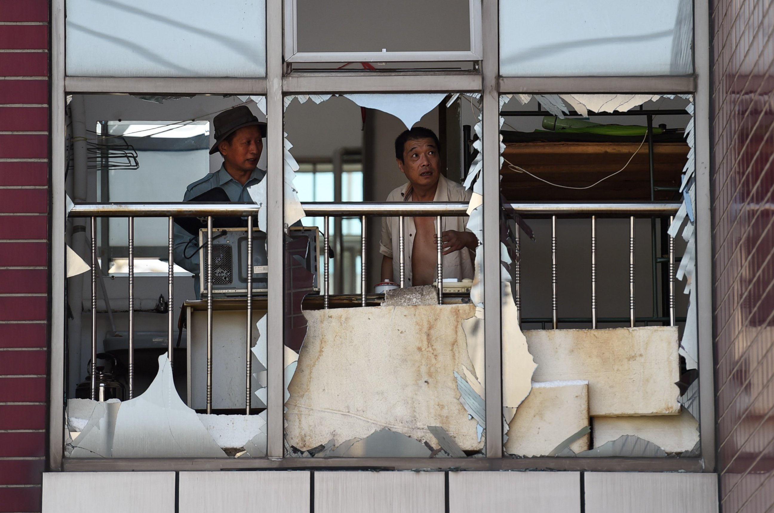 PHOTO: Two men look at broken windows in a building near the site of an explosion in Tianjin, China on Aug. 13, 2015.    