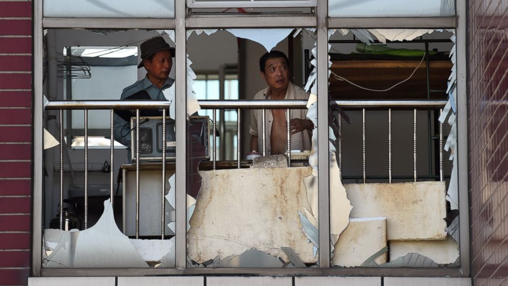 PHOTO: Two men look at broken windows in a building near the site of an explosion in Tianjin, China on Aug. 13, 2015.    