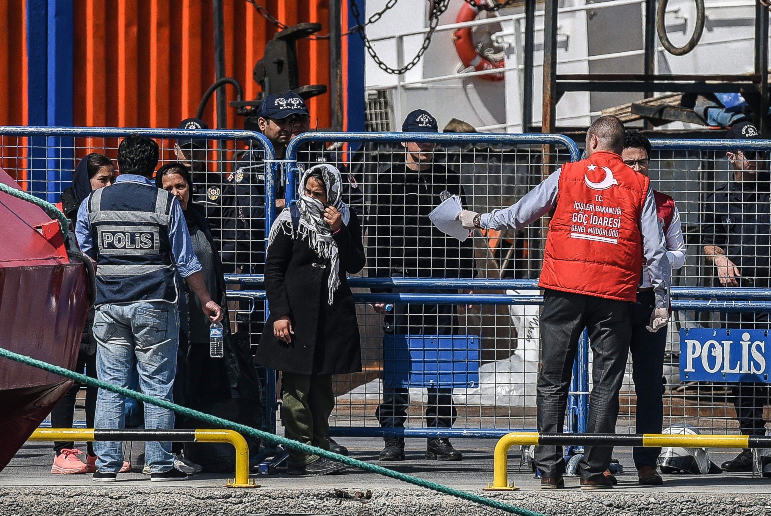 PHOTO: A Turkish police officer escorts deported women migrants from a small Turkish ferry carrying migrants who are deported to Turkey on April 4, 2016 as they arrive at the port of Dikili district in Izmir.  