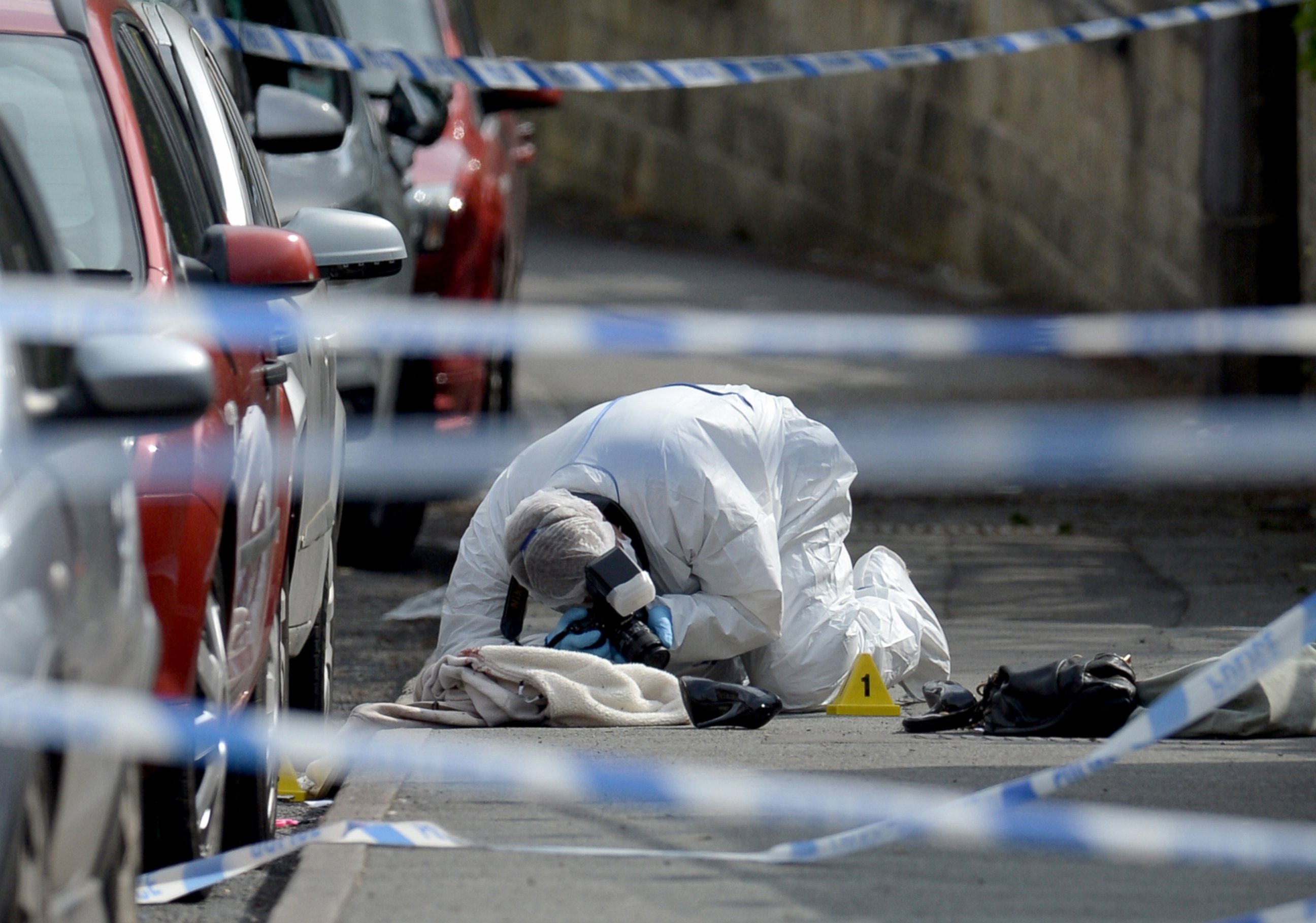PHOTO: A police forensic officer works at the scene where a coat, shoe and handbag lie on the pavement outside the library in Birstall where Labour MP Jo Cox was shot, June 16, 2016.