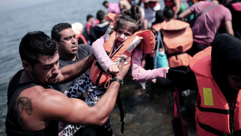 PHOTO: A refugee carries a child as they arrive on the shores of the Greek island Lesbos in an inflatable dingy across the Aegean Sea from from Turkey, Sept. 3, 2015.  