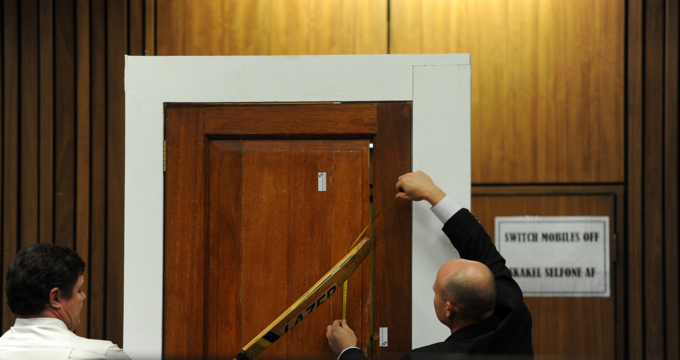 PHOTO: Forensic investigator Johannes Vermeulen, left, takes part in the reconstruction of hitting a door with a cricket bat during the trial of Oscar Pistorius in Pretoria, South Africa on March 12, 2014. 