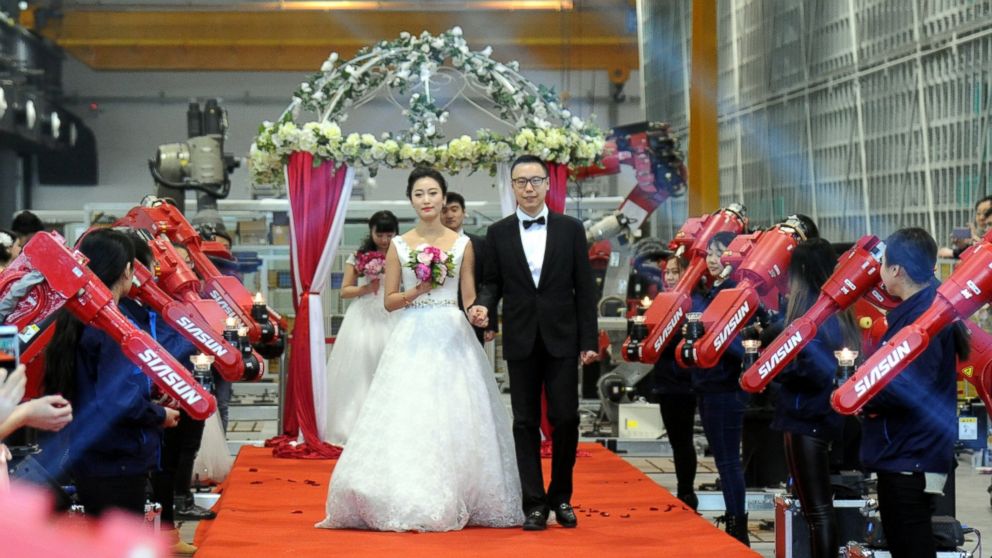Couples walk on a red carpet between two rows of red robots waving the burning candles up and down during a group wedding ceremony at a robot factory, Jan. 20, 2016, in Shenyang, China. 