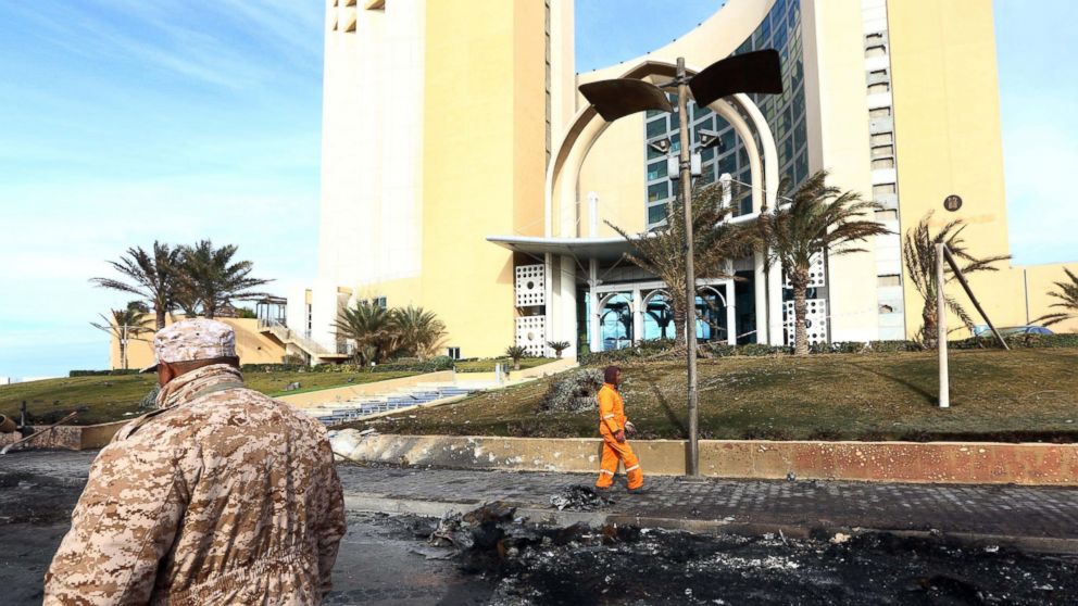 PHOTO: A member of security, left, for Tripoli's central Corinthia Hotel looks on as sanitation workers clean the debris outside the hotel on Jan. 28, 2014.