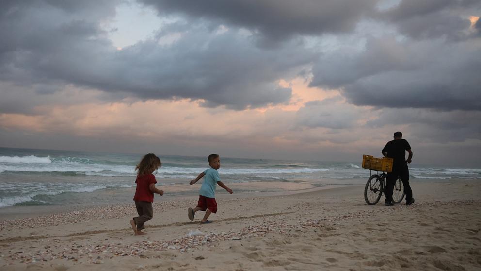 PHOTO: Displaced Palestinian children run behind a man pushing his bicycle on the sand at sunrise at a makeshift camp by the beach in Al-Zawayda city, near Deir al-Balah, in the central Gaza Strip on Oct. 9, 2025.