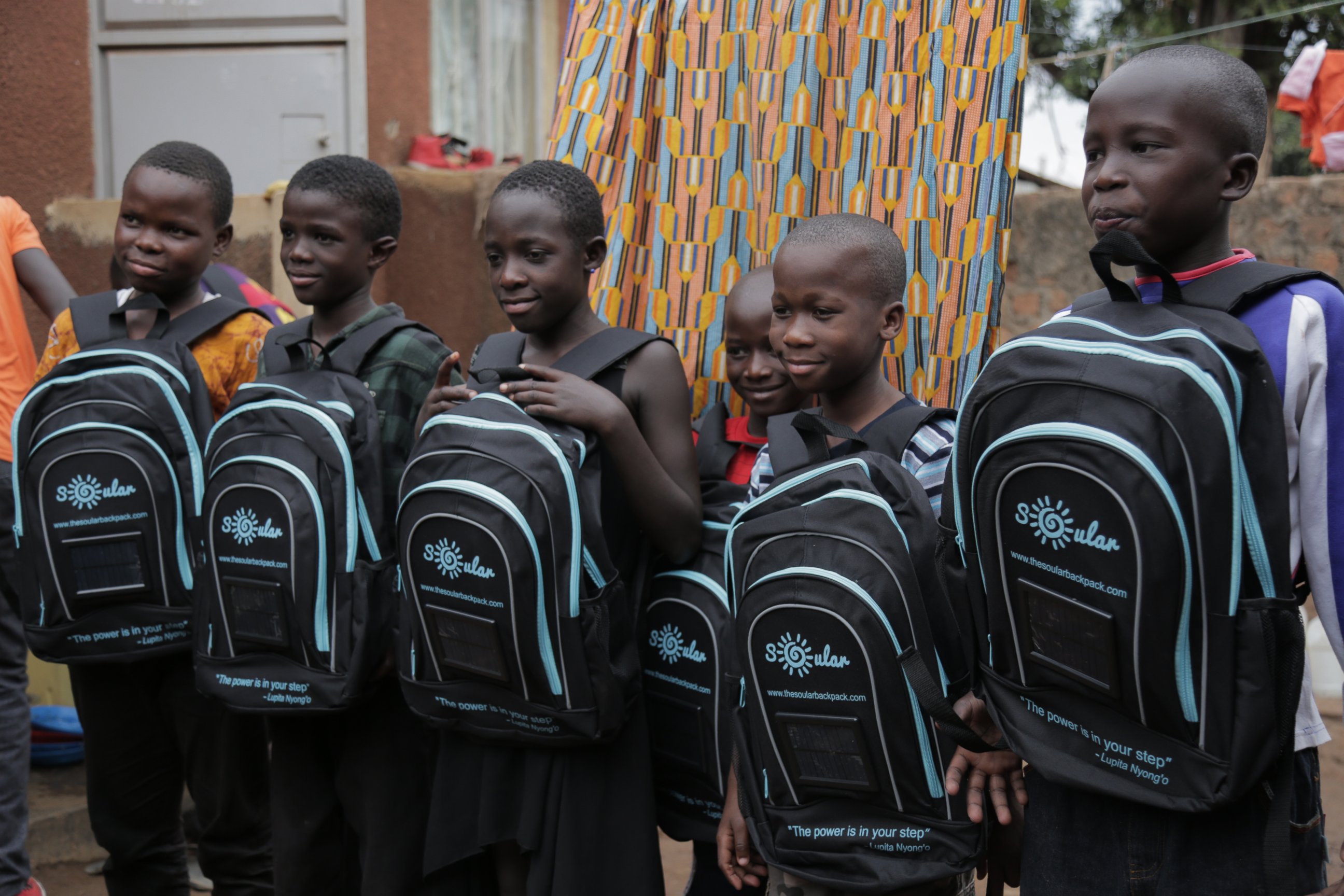 PHOTO: Local children pose with solar panel equipped backpacks from the Soular Backpack that launched in 2015 to allow children take control of their education, Katwe, Uganda.  
