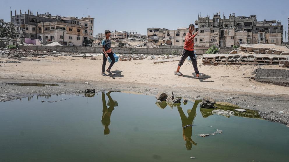 PHOTO: Two Palestinian boys walk past stagnant pools of water in Khan Yunis in the southern Gaza Strip on July 19, 2024,
