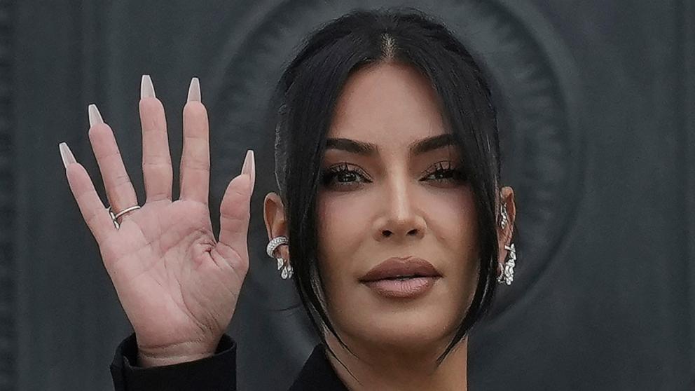 PHOTO: Kim Kardashian waves as she arrives to testify regarding a robbery of millions of dollars in jewels from her Paris hotel room in 2016, in Paris, May 13, 2025. 