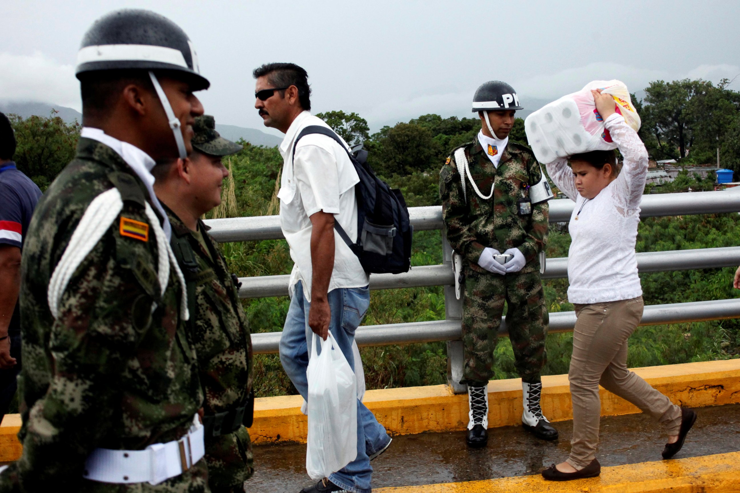 PHOTO: A young woman carries toilet paper as she crosses the Colombian-Venezuelan border over the Simon Bolivar international bridge after shopping while a Colombian police officer looks on in Cucuta, Colombia, July 16, 2016. 