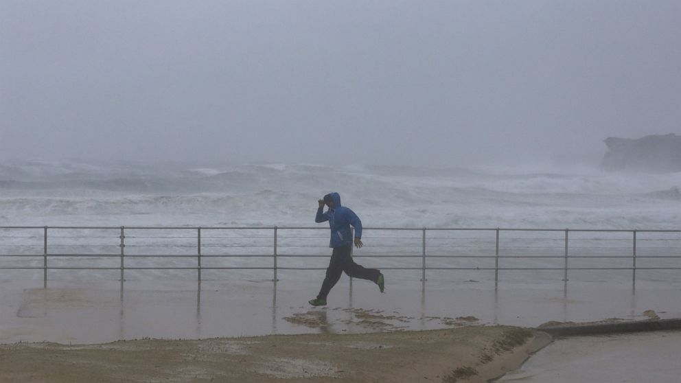 PHOTO: A man runs past heavy seas as sand is blown inland by heavy winds at Sydney's Bondi Beach