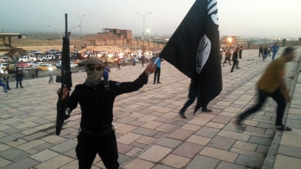 PHOTO: A fighter of the Islamic State of Iraq and the Levant (ISIL) holds an ISIL flag and a weapon on a street in the city of Mosul, June 23, 2014.