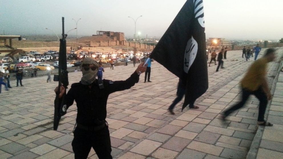 A fighter of the Islamic State of Iraq and the Levant (ISIL) holds an ISIL flag and a weapon on a street in the city of Mosul, June 23, 2014. 