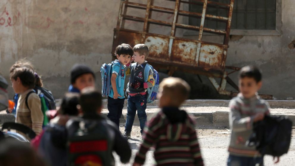 Children carrying school bags stand near the Nabaa Al-Hayat center for education and psychosocial support for children in places undergoing a crisis, in eastern al-Ghouta, near Damascus, Oct. 21, 2014.