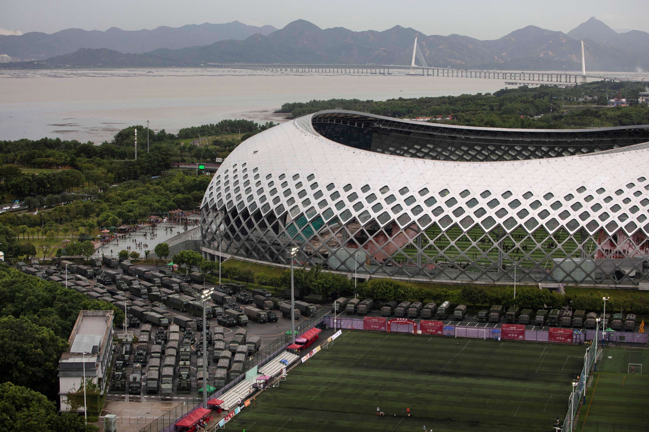 PHOTO: Armored vehicles and troop trucks are parked in a lot by Shenzhen Bay Stadium with the Shenzhen Bay Bridge that connects to Hong Kong in the background, Aug. 17, 2019, in Shenzhen, China.