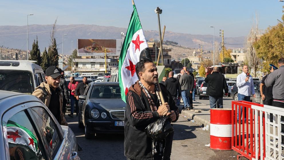 PHOTO: A man carries a Syrian opposition flag as he walks at the Lebanese Masnaa border crossing on the way to Syria on Dec. 9, 2024.