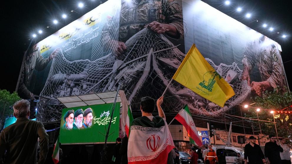 PHOTO: An Iranian demonstrator waves a flag of Lebanon's militant Hezbollah group under an anti-U.S. billboard in Tehran, Iran, on May 4, 2026.