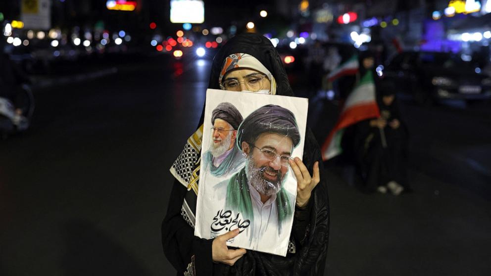 PHOTO: A woman holds a placard with photos of Iran's Supreme Leader Ayatollah Mojtaba Khamenei and his predecessor and late father Ayatollah Ali Khamenei during a protest at the Hafte Tir Square in Tehran on May 17, 2026.