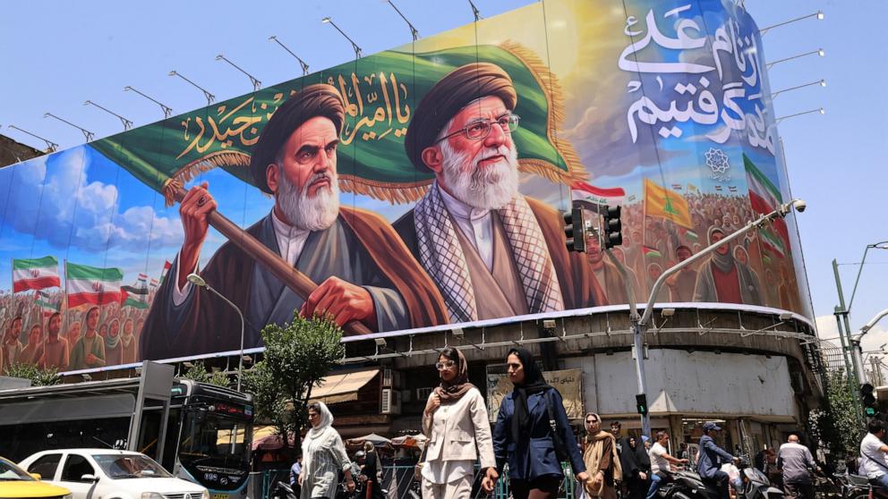 PHOTO: People cross the street past a large billboard showing portraits of Iran's late Supreme Leader Ayatollah Ruhollah Khomeini (L) and slain Supreme Leader Ayatollah Ali Khamenei (R) in central Tehran on June 8, 2026.