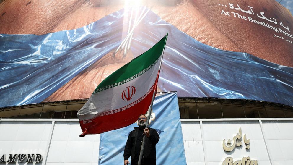 PHOTO: A man holds an Iranian flag near an anti-U.S. billboard in Tehran, Iran, on May 2, 2026.
