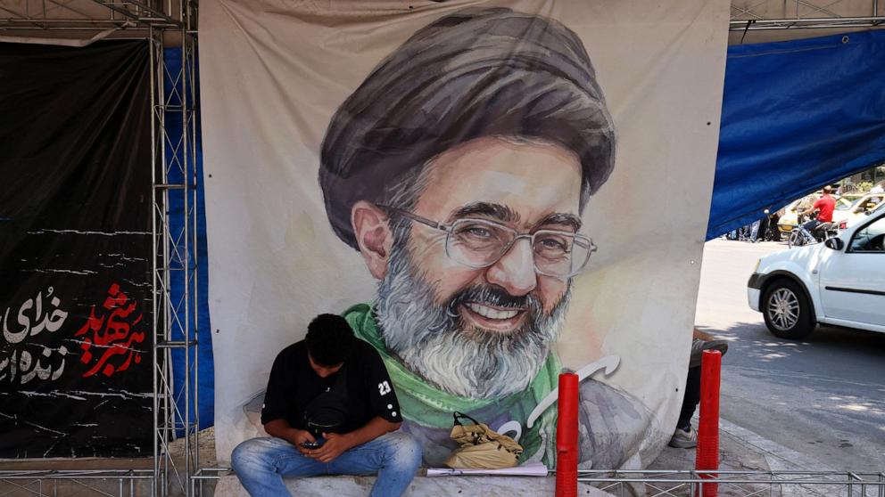 PHOTO: A man sits in front of a poster with portrait of Iranian Supreme Leader Mojtaba Khamenei, in Vanak Square in Tehran, on June 10, 2026.