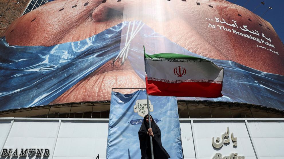 PHOTO: A woman holds an Iranian flag near an anti-U.S. billboard depicting U.S. President Donald Trump and the Strait of Hormuz, in Tehran, Iran, on May 25, 2026.