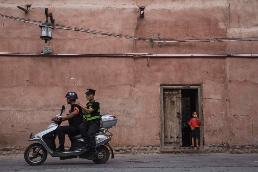 PHOTO: Police patrol on a scooter as an ethnic Uyghur boy stands in his doorway,June 27, 2017, in the old town of Kashgar, in the far western Xinjiang province, China. 