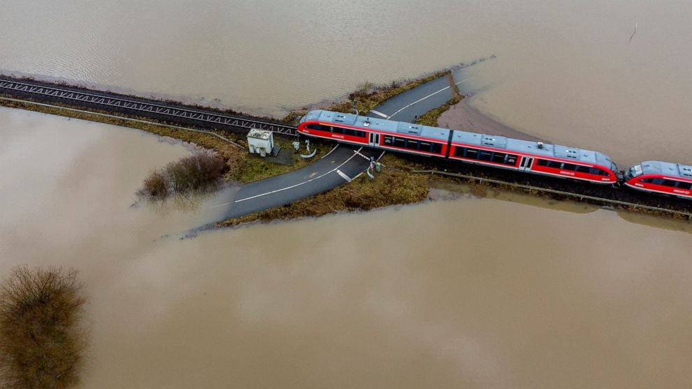A train passes a rail road crossing that is surrounded by flooding caused by rain and melting snow in Nidderau near Frankfurt, Germany, Wednesday, Feb. 3, 2021. (AP Photo/Michael Probst)