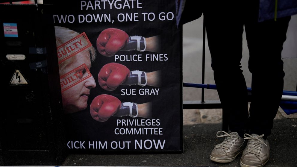 FILE - An anti-Boris Johnson, anti-Brexit protester stands next to a placard across the street from the Houses of Parliament on the edge of Parliament Square, in London, Wednesday, May 25, 2022. Johnson was dealt a major blow Tuesday, July 5, 2022 wh