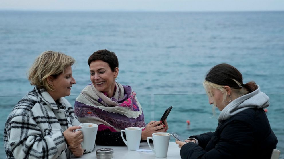 Nadine Kalache Maalouf, center, Celine Elbacha and Elbacha's daughter Morgane, right, sit at a seaside restaurant in the eastern coastal resort of Paralimni, Cyprus, Wednesday, Dec. 22, 2021. They are among the thousands of Lebanese, including teache