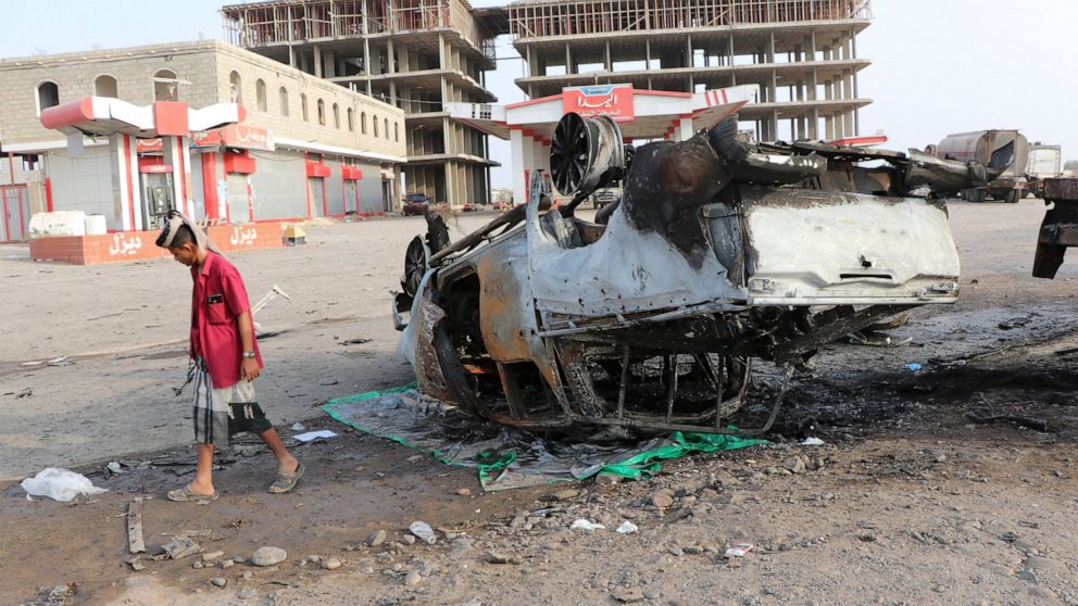 An armed man walks next to a destroyed vehicle at the site of a deadly car bomb attack in the port city of Aden, Yemen, Thursday, Mar. 24, 2022. A car bomb rocked Yemen's southern city of Aden on Wednesday, killing a senior military official and at l