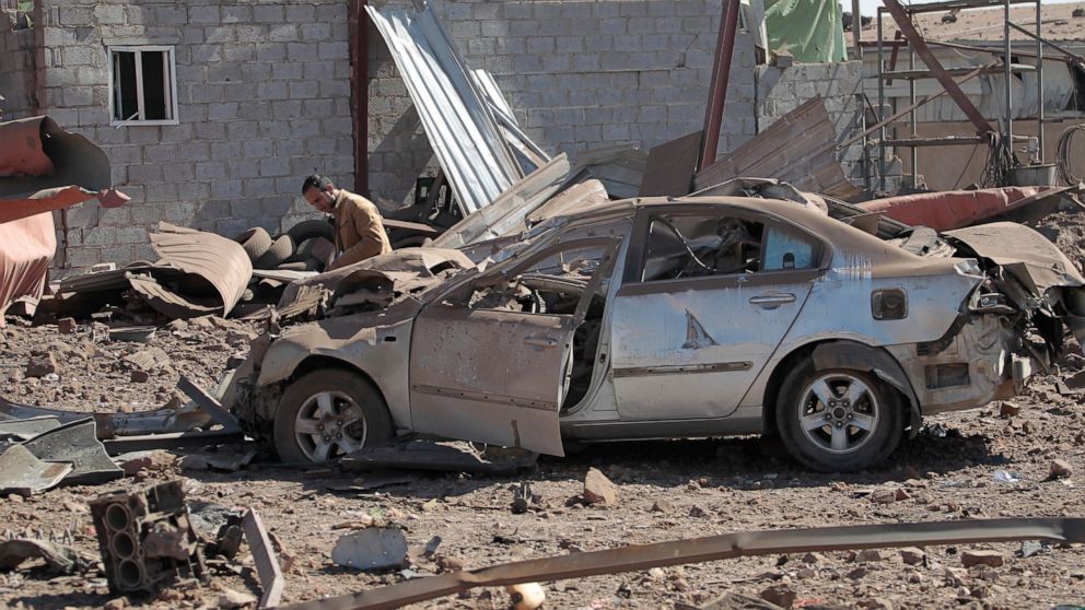 A man inspects a damaged car at the site of airstrikes by a Saudi-led coalition on a workshop, in Sanaa, Yemen, Sunday, Dec. 5, 2021. The coalition fighting Iran-backed rebels in Yemen accelerated airstrikes on the capital and elsewhere in the confli