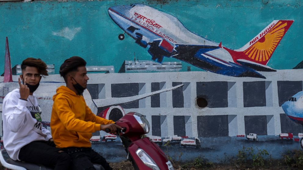 FILE - A scooterist drives past a wall painted with Air India planes in Mumbai, India, Thursday, Jan. 27, 2022. India's oldest and largest conglomerate Tata Sons will merge its Air India with Vistara, which it jointly runs with Singapore Airlines, ac