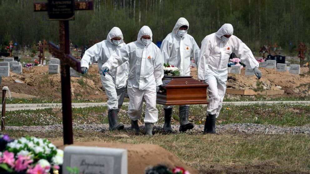 FILE - In this May 15, 2020, file photo, gravediggers in protective suits carry the coffin of a COVID-19 victim as relatives and friends stand at a distance in the section of a cemetery reserved for coronavirus victims in Kolpino, outside St. Petersb