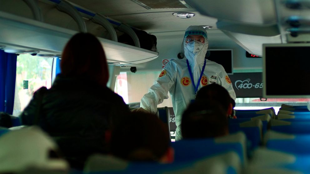 A government worker in full protective gear speaks on a bus to passengers recently arrived from Wuhan about an imminent medical screening in Beijing, China, Wednesday, April 15, 2020. Wuhan, the city at the center of the global coronavirus epidemic, 