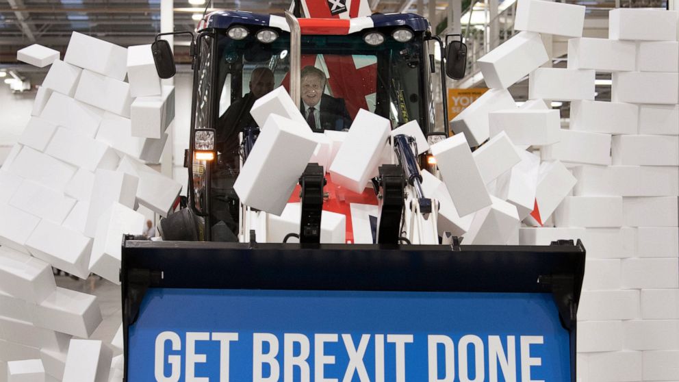 Britain's Prime Minister Boris Johnson sits in the cab to break through a symbolic wall with the Conservative Party slogan 'Get Brexit Done', during an election campaign event at the JCB manufacturing facility in Uttoxeter, England, Tuesday Dec. 10, 