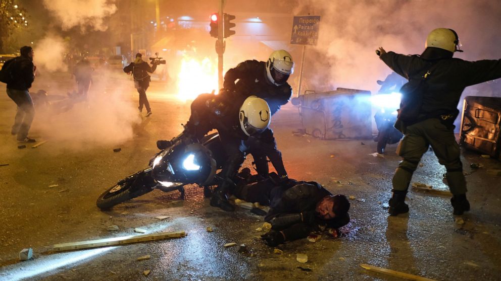 A policeman lays injured on the road after an attack by protesters as his colleagues try to help him during clashes in Athens, Tuesday, March 9, 2021. Severe clashes broke out Tuesday in Athens after youths protesting an incident of police violence a