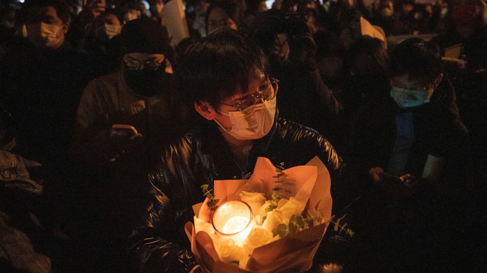 A protester holds flower and candles in Beijing, Sunday, Nov. 27, 2022. Protesters angered by strict anti-virus measures called for China's powerful leader to resign, an unprecedented rebuke as authorities in at least eight cities struggled to suppre
