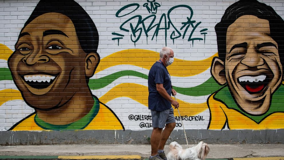 A man walks his dog past a mural of Brazilian soccer stars Pele, left, and Garrincha in Rio de Janerio, Brazil, Friday, Dec. 30, 2022. Edson Arantes do Nascimento, known to the world as Pele, died in Sao Paulo Thursday at the age of 82. (AP Photo/Bru