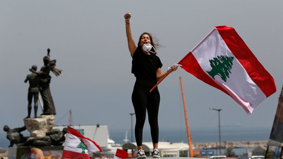 An anti-government protester stands on the top of her car shouting slogans and waving the Lebanese flag, during driving protest through the streets to express rejection of the political leadership they blame for the economic and financial crisis, in 