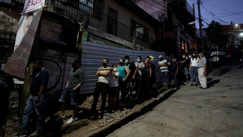 People line up outside a polling station after closing time to vote during general elections in Tegucigalpa, Honduras, Sunday, Nov. 28, 2021. The National Electoral Council announced that polling stations that still had people waiting outside to vote