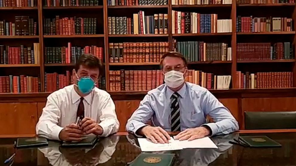 In this handout photo released by Brazil's Presidential Press Office, Brazilian Health Minister Luiz Henrique Mandetta, left, and President Jair Bolsonaro, wear masks as they speak about the new coronavirus during a Facebook Live transmission, in Bra