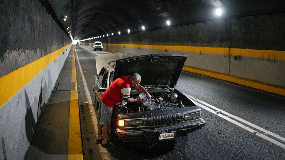 A man tries to cool down his overheating car by pouring water into the radiator, in one of the tunnels of the road that connects La Guaira with Caracas, Venezuela, Tuesday, April 19, 2022. Drivers try to coax a little more life out of aging vehicles 