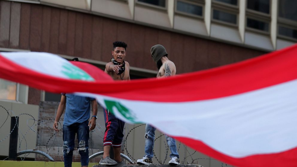 Anti-government protesters stand on a concrete wall that installed by authorities to block a road leading to the parliament building and shout slogans during ongoing protests against the Lebanese government in Beirut, Lebanon, Sunday, June 14, 2020. 