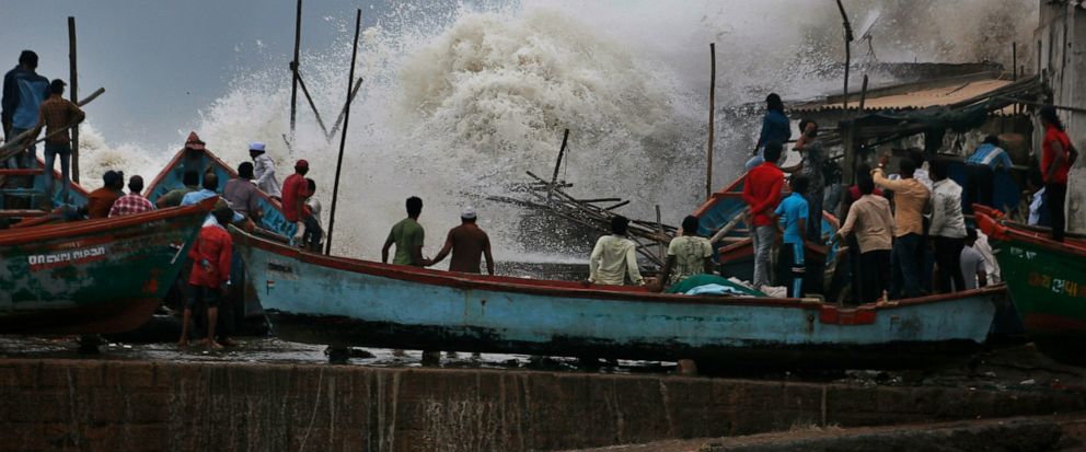 A waves crashes as people stand on boats on the Arabian Sea coast in Veraval, Gujarat, India, Wednesday, June 12, 2019. Indian authorities evacuated tens of thousands of people on Wednesday as a severe cyclone in the Arabian Sea approached the wester
