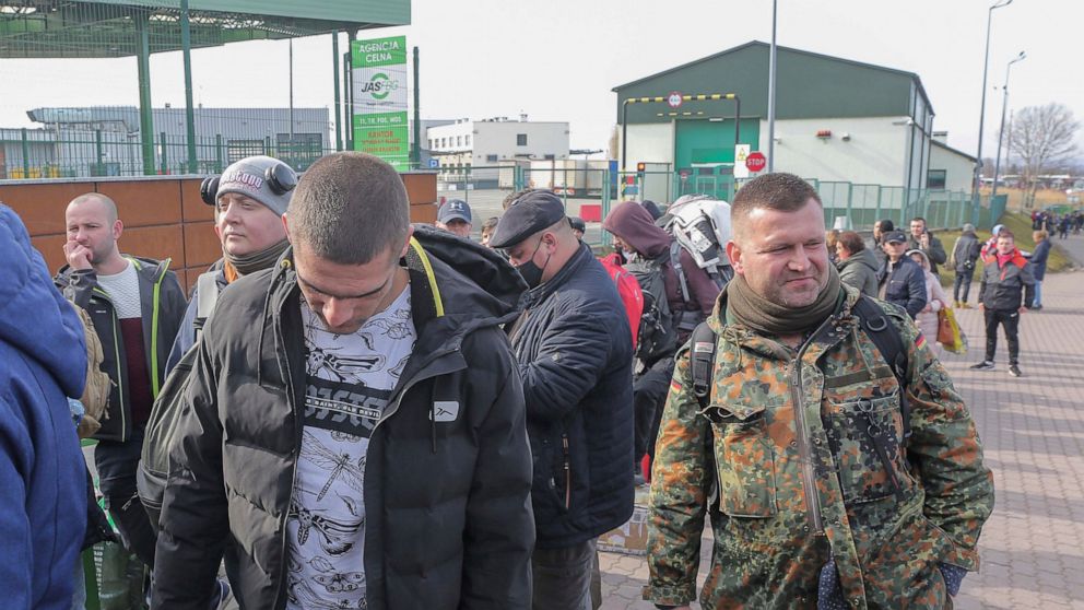 Polish volunteer Jedrzej, 34, in military uniform joins Ukranians, left, waiting to cross the border to go and fight against Russian forces, at Medyka border crossing, in Poland, Saturday, Feb. 26, 2022. (AP Photo/Visar Kryeziu)