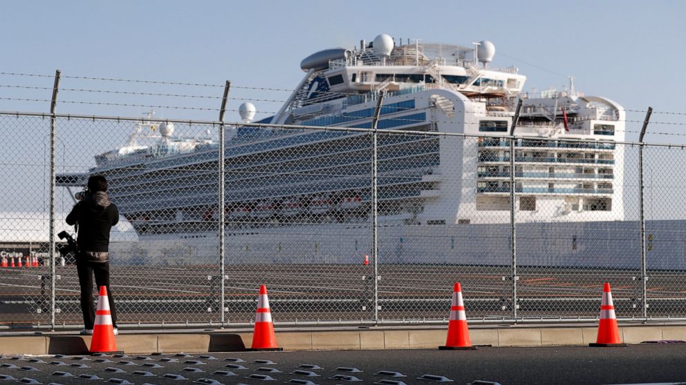 A photographer takes photos near the quarantined Diamond Princess cruise ship anchored at a port in Yokohama, near Tokyo, Friday, Feb. 21, 2020. Passengers tested negative for COVID-19 started disembarking since Wednesday. (AP Photo/Eugene Hoshiko)