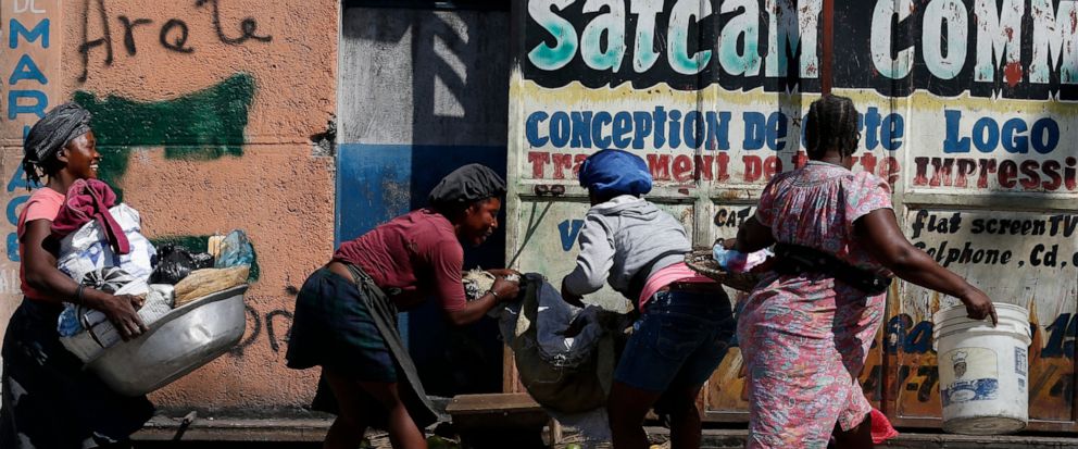 Vendors scramble to pack up their goods and get inside, as protesters calling for President Jovenel Moïse march up a road in downtown Port-au-Prince, Haiti, Monday, Oct. 21, 2019. Anger over corruption, inflation and scarcity of basic goods including